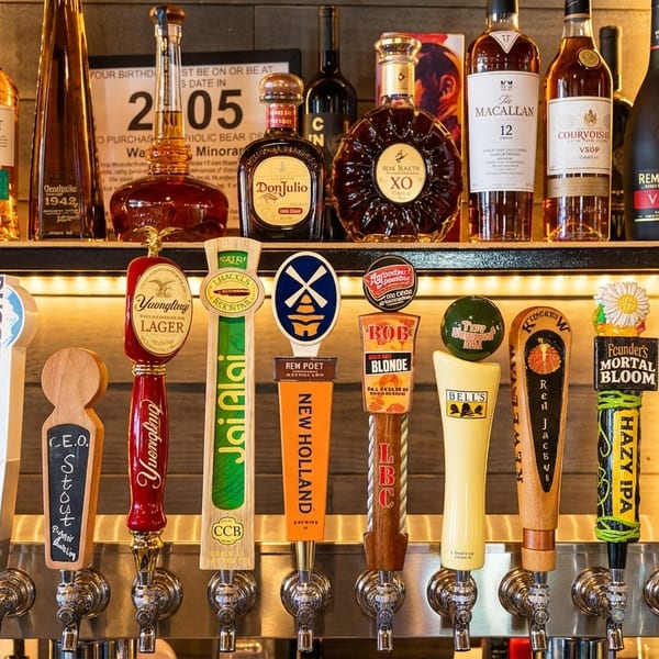 A bar tap with various beer handles and liquor bottles on shelves in the background.