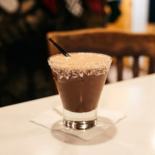 Chocolate cocktail with a salt-rimmed glass and a black straw on a white table.