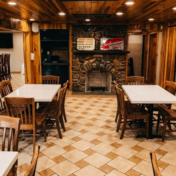 Cozy restaurant interior with wood paneling, tiled floor, white tables, wooden chairs, and a stone fireplace.