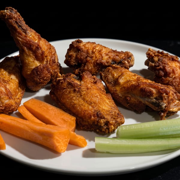 Crispy fried chicken wings with carrot and celery sticks on a white plate.