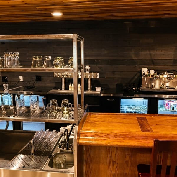 A well-equipped bar area with a wooden counter, glass shelves, beer taps, and espresso machine.